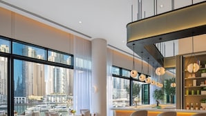 A modern hotel interior with large windows offering city views, a bar area with stools, and a seating area with chairs. - Vida Residences Dubai Marina (Dubai)