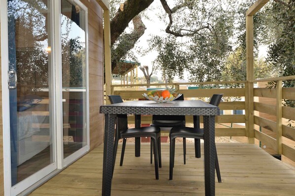 A wooden deck with a table and chairs, a glass door, and a view of trees.