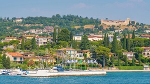 A coastal town with a historic castle on a hill, residential buildings, and a marina with boats. - Mobilehome with terrace, pool and air conditioning (Padenghe sul Garda)