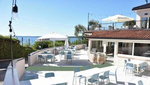 An outdoor patio with tables and chairs, a bar area, and a view of the sea. - Mobilehome with terrace, pool and air conditioning (Padenghe sul Garda)