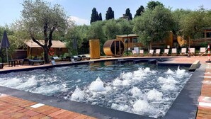 A swimming pool with water jets, surrounded by lounge chairs and a wooden deck. - Mobilehome with terrace, pool and air conditioning (Padenghe sul Garda)