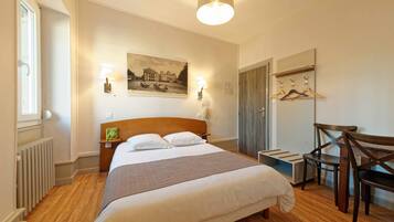 Une chambre bien rangée, avec un grand lit, des lampes de chevet, une tête de lit en bois, un radiateur, une chaise en bois, un porte-manteau et un tableau encadré au mur.