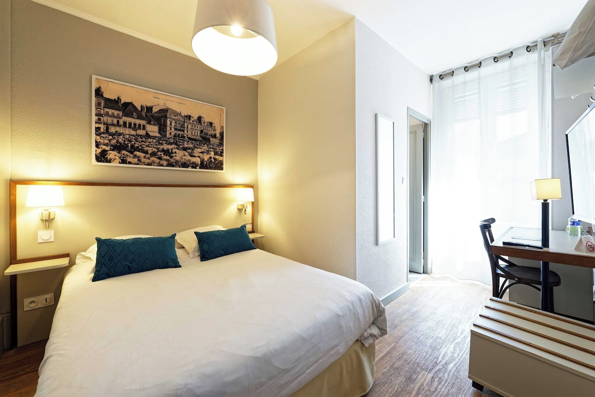 Une chambre d’hôtel avec un grand lit, deux lampes de chevet, un bureau avec une chaise et une fenêtre avec des rideaux.