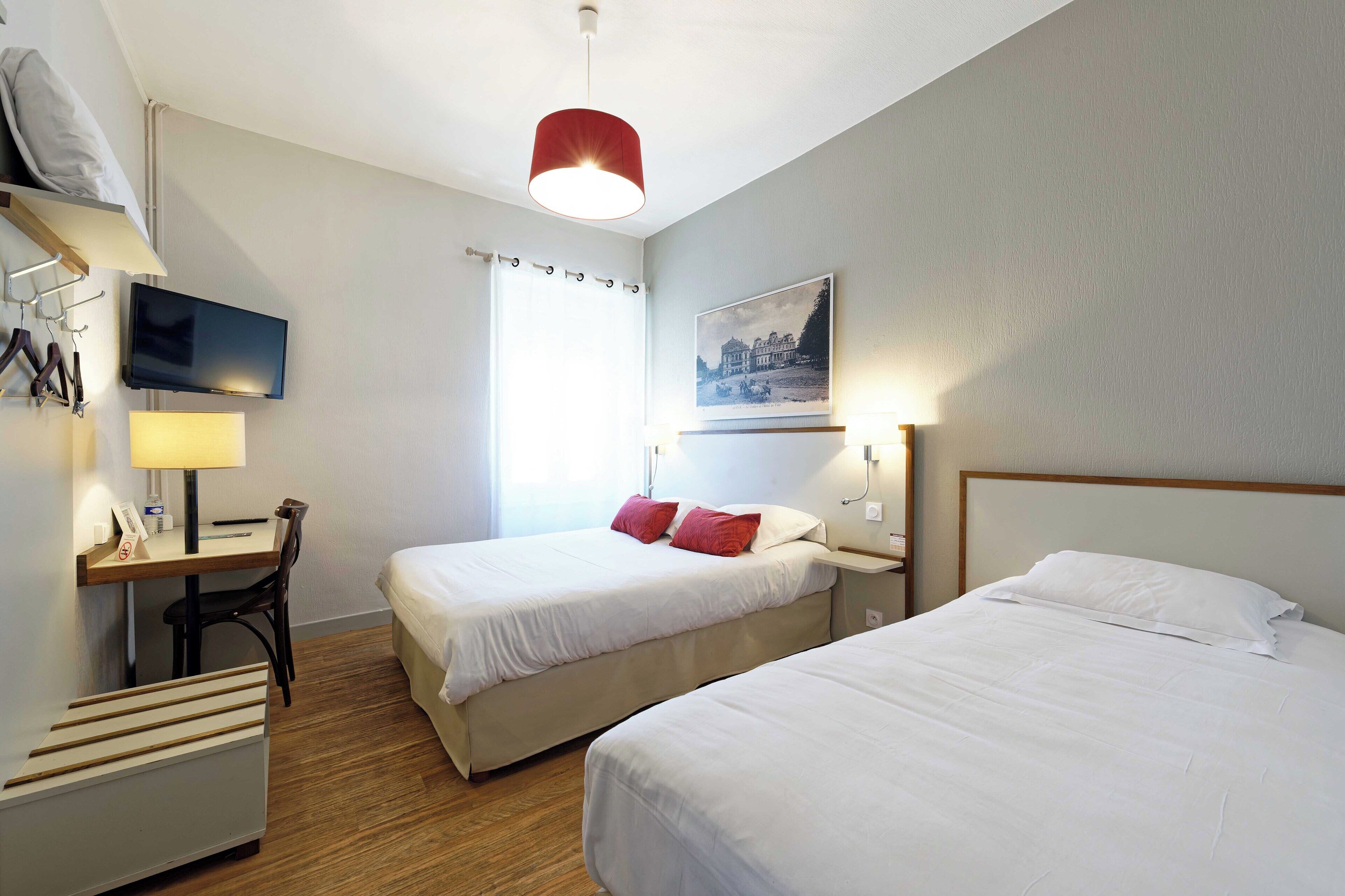 Une chambre d’hôtel avec deux lits, un bureau avec une chaise, une télévision et un tableau au mur.