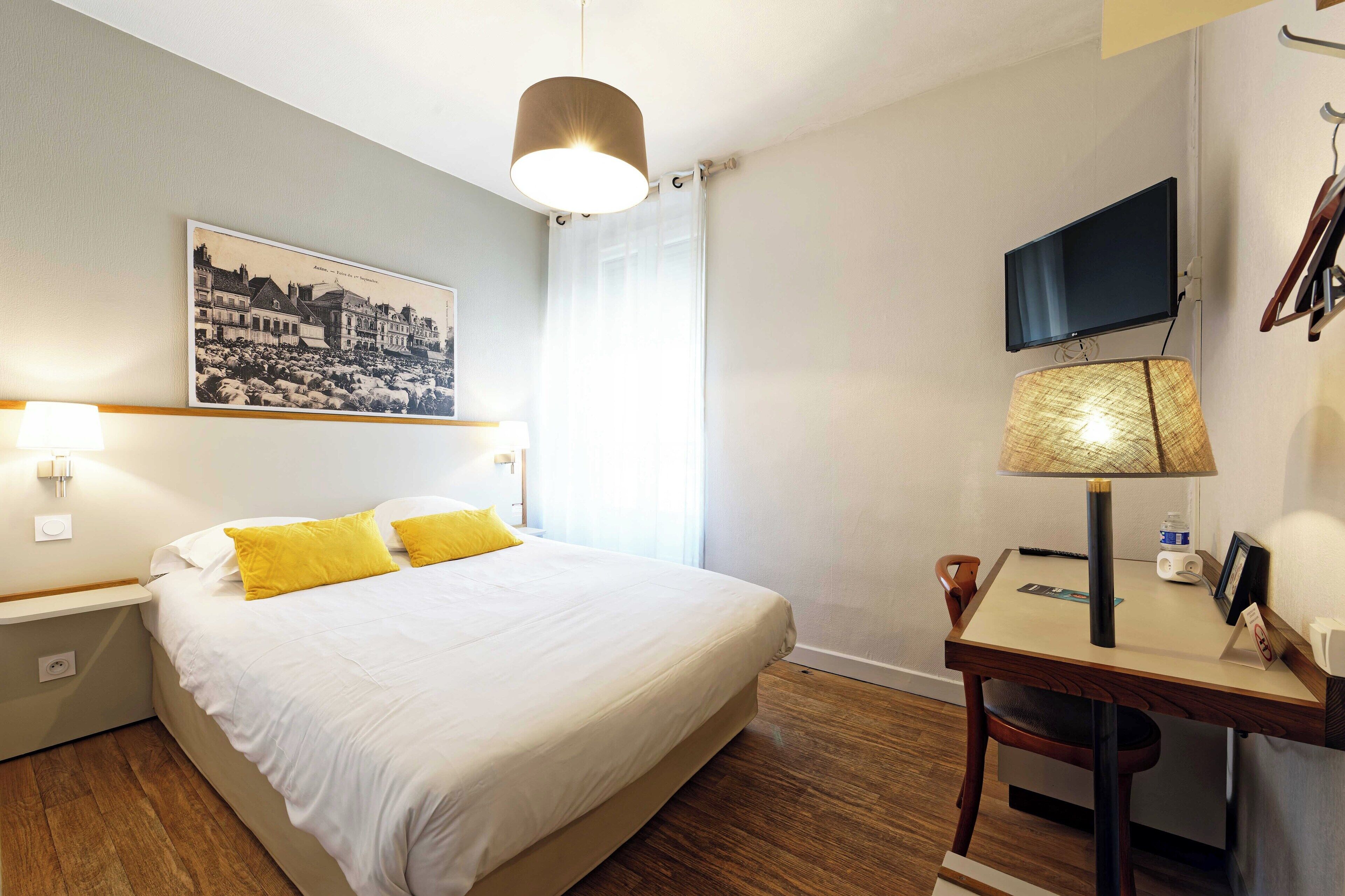 A hotel room with a bed, a desk with a lamp, a television, and a picture on the wall.