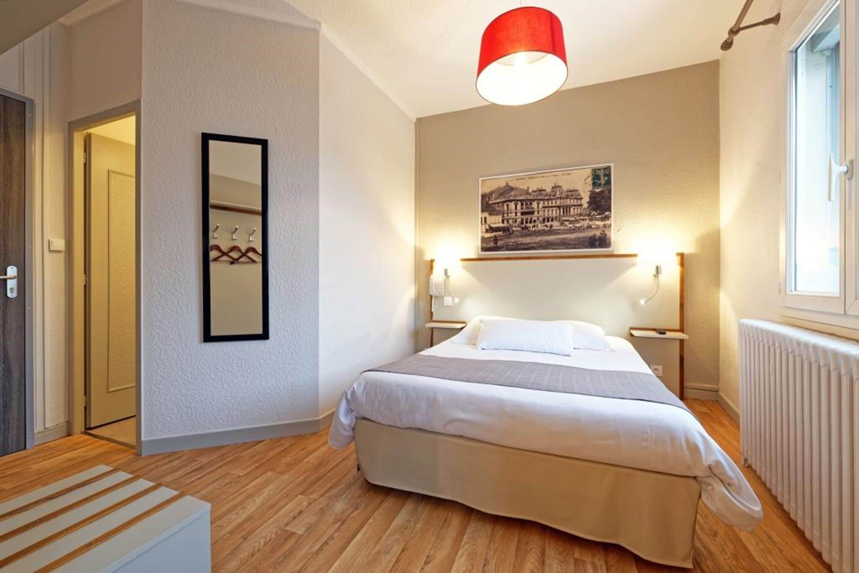 A bedroom with a bed, a mirror, a picture on the wall, and a window.