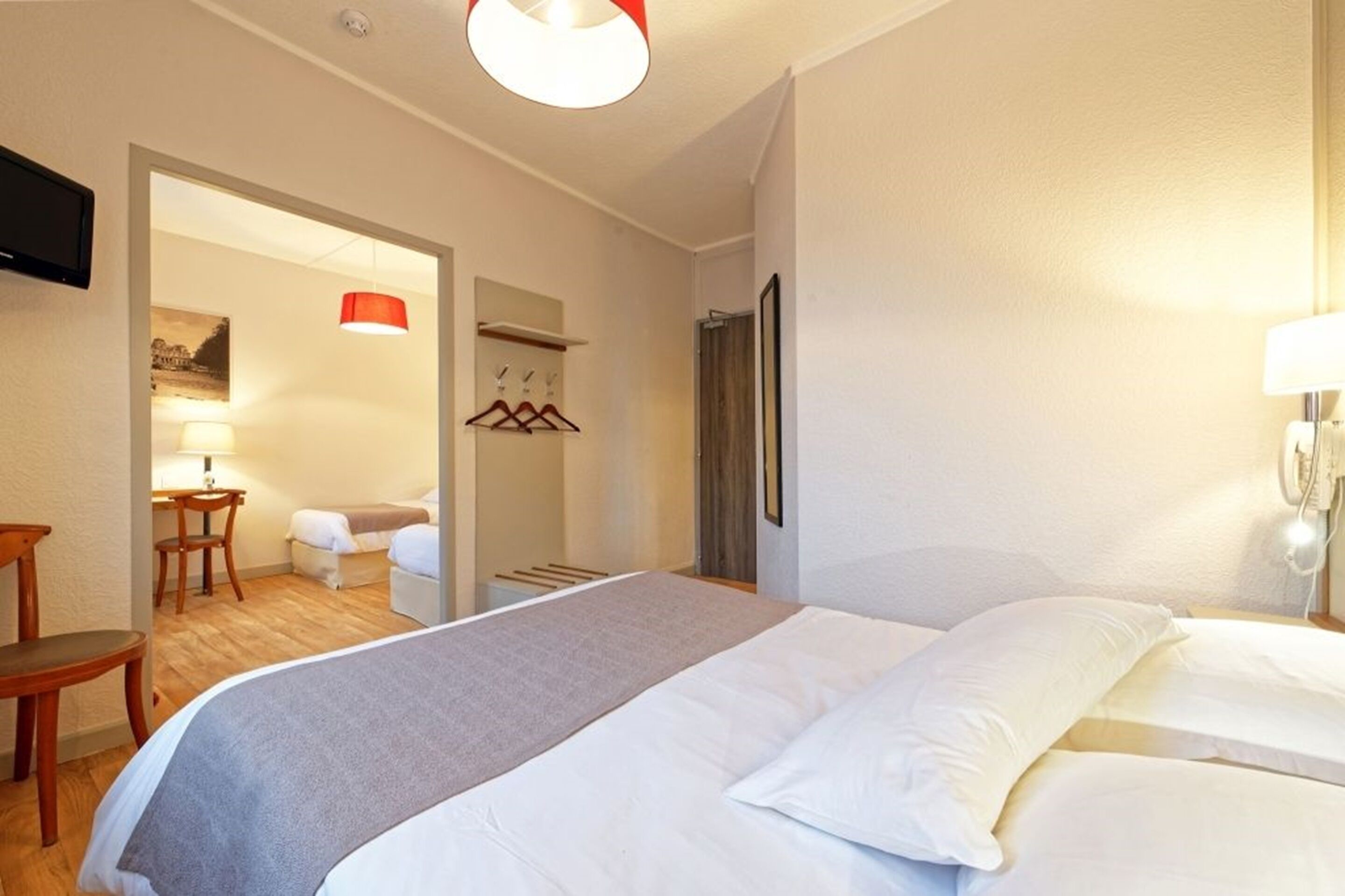 A hotel room with a bed, a desk, a chair, a TV, and a bathroom visible through an open door.
