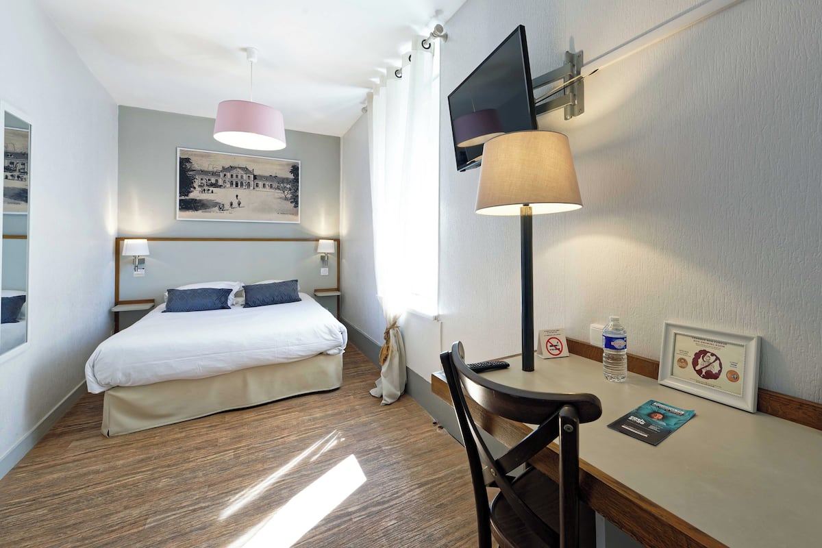 Une chambre d’hôtel équipée d’un lit, d’un bureau, d’une chaise, d’une lampe, d’une télévision et d’un certificat encadré accroché au mur.