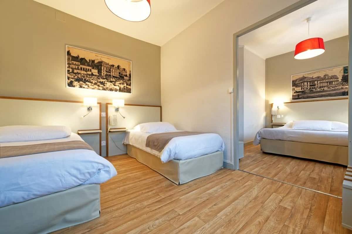 Une chambre d’hôtel avec trois lits, un plancher en bois et deux lampes fixées au mur.