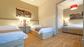 Camera d'albergo con tre letti, pavimento in legno e due lampade a parete.