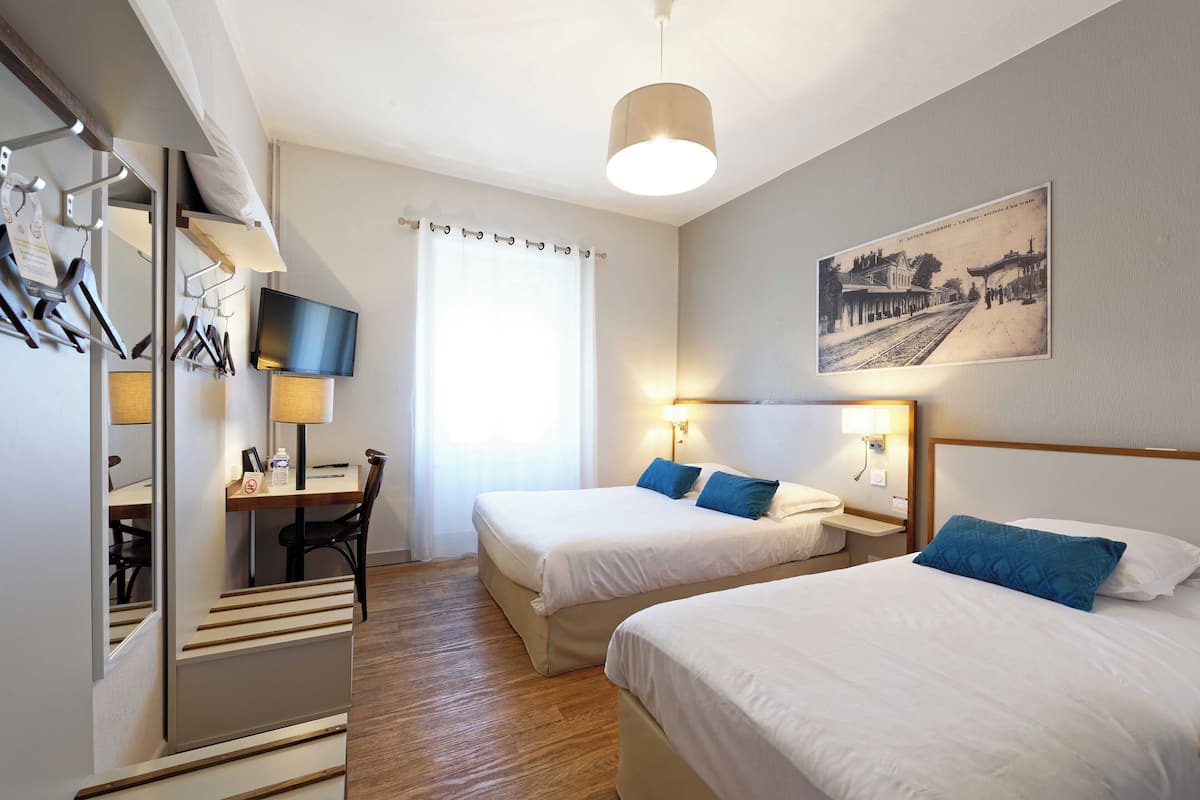 Une chambre d’hôtel avec deux lits, un bureau avec une chaise, une télévision et un tableau au mur.