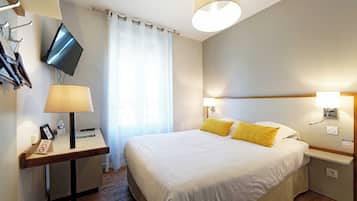 Una camera d'hotel con un letto, lampade sui comodini, una TV a parete, una scrivania con il telefono e una finestra con tende.