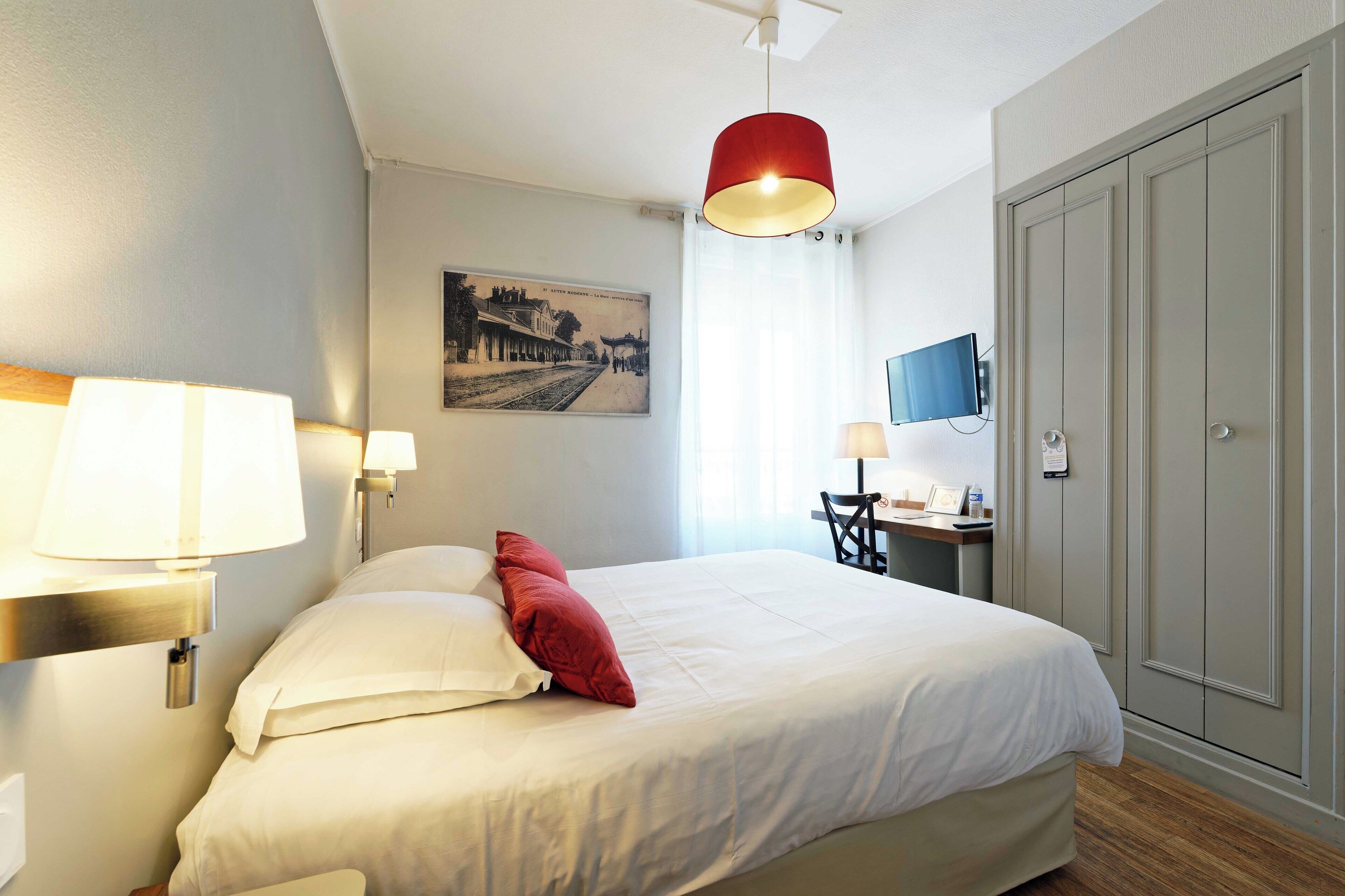 Una habitación de hotel con cama, escritorio, silla, televisor y armario.