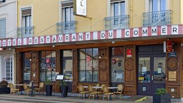 A hotel with outdoor seating and a sign reading "HOTEL RESTAURANT DU COMMER".