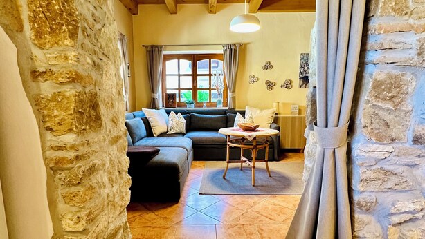 A cozy living room with a stone wall, wooden ceiling beams, a sofa, and a table.