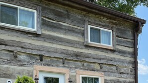 Une cabane rustique en rondins de bois, dotée d’une porte d’entrée, de deux fenêtres et d’un petit porche.