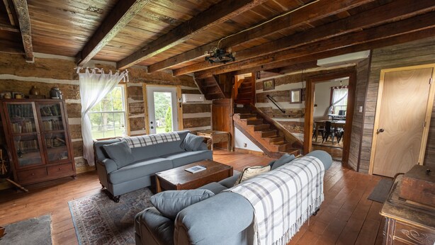 L’intérieur d’une cabane en rondins, avec un canapé, une table basse, une cheminée et un escalier menant à une autre pièce.