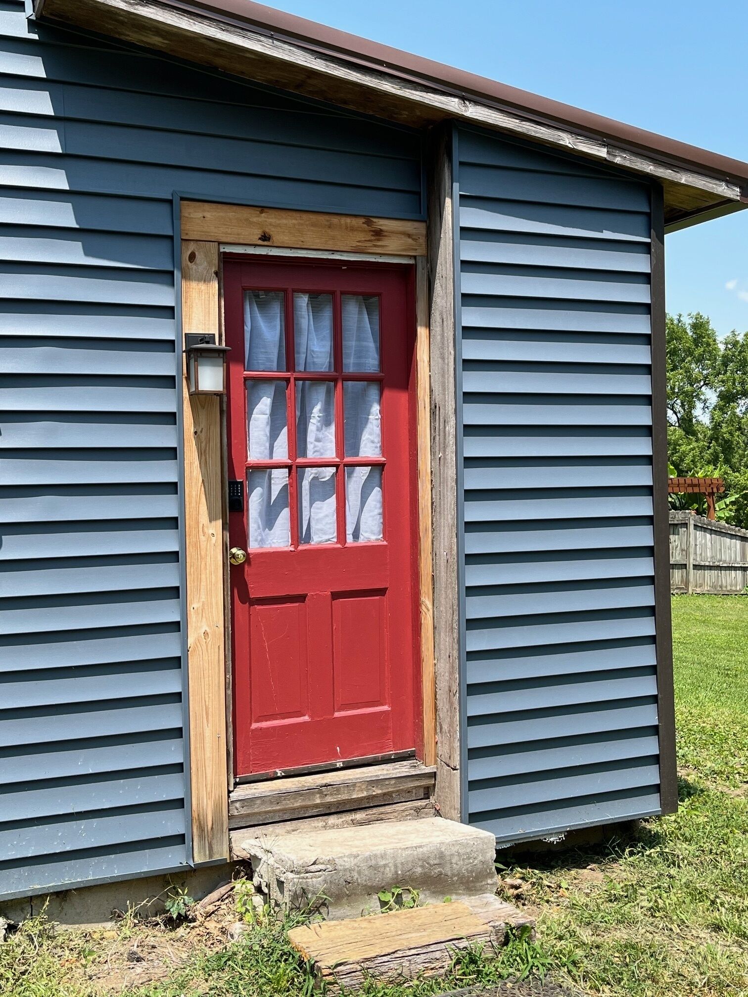 A small, single-story building with a red door and a wooden step leading to the entrance.