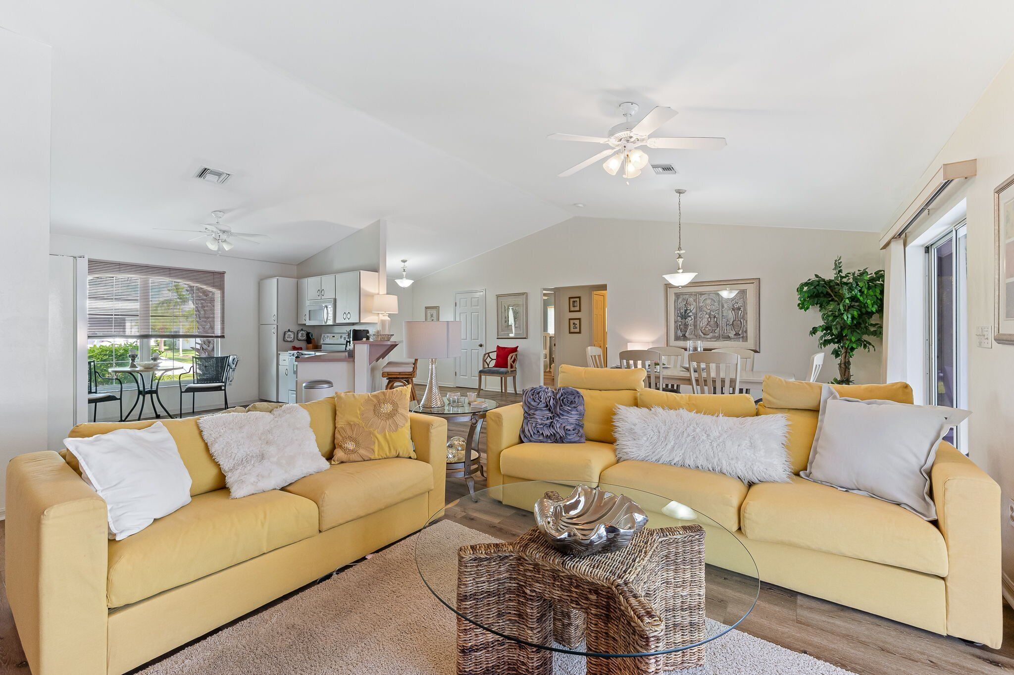 A spacious living room with two yellow sofas, a glass coffee table, and a ceiling fan.
