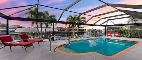 An outdoor swimming pool with red lounge chairs and a covered area.