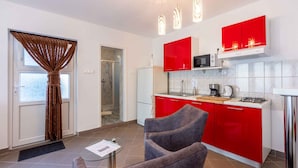 A modern kitchen with red cabinets, a microwave, and a gas stove. There is a glass table with a chair in the foreground. - Studio with a large terrace (Novi Vinodolski)