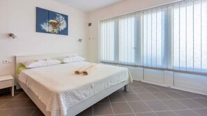 A hotel room with a bed, a nightstand, a wall-mounted lamp, and a large window with blinds. - Studio with a large terrace (Novi Vinodolski)