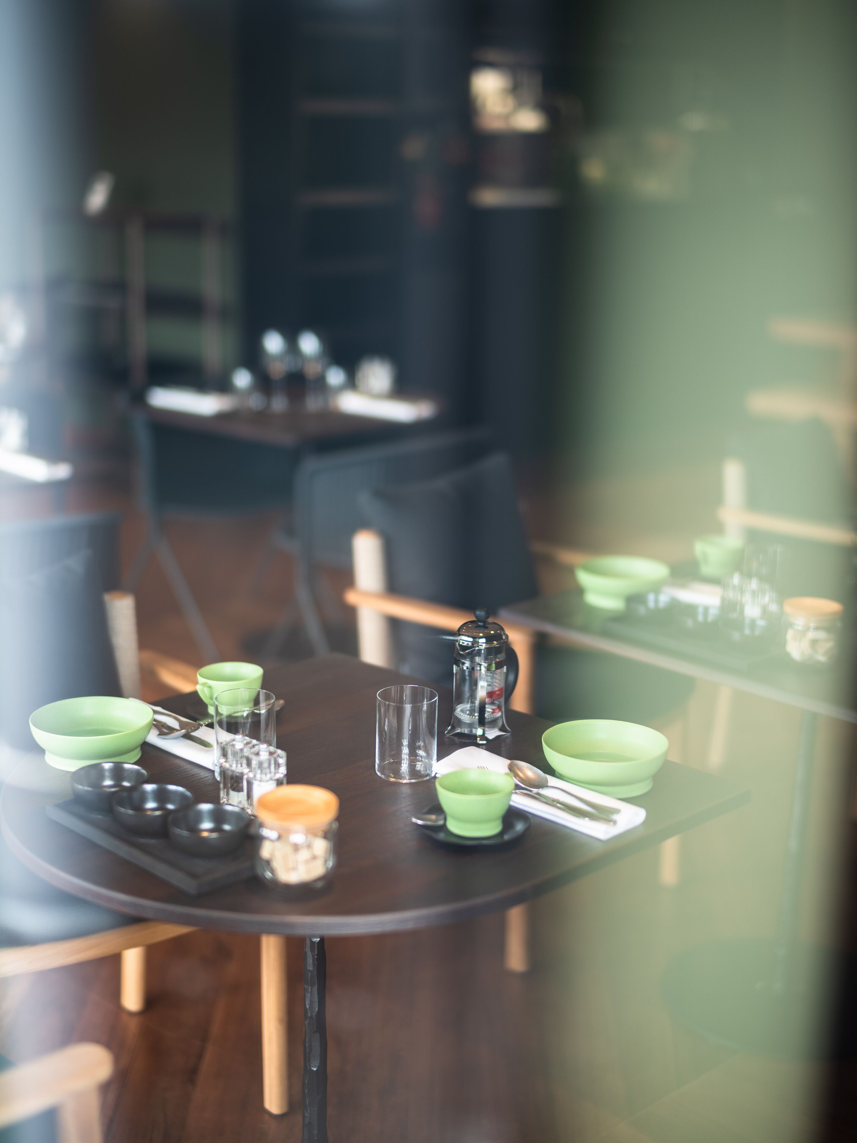 A dining table set with green bowls, glasses, and a coffee pot.