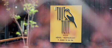 Placa de hotel com logotipo de pássaro e o nome 'TUIT TUIT HOTEL RESTAURANT'.