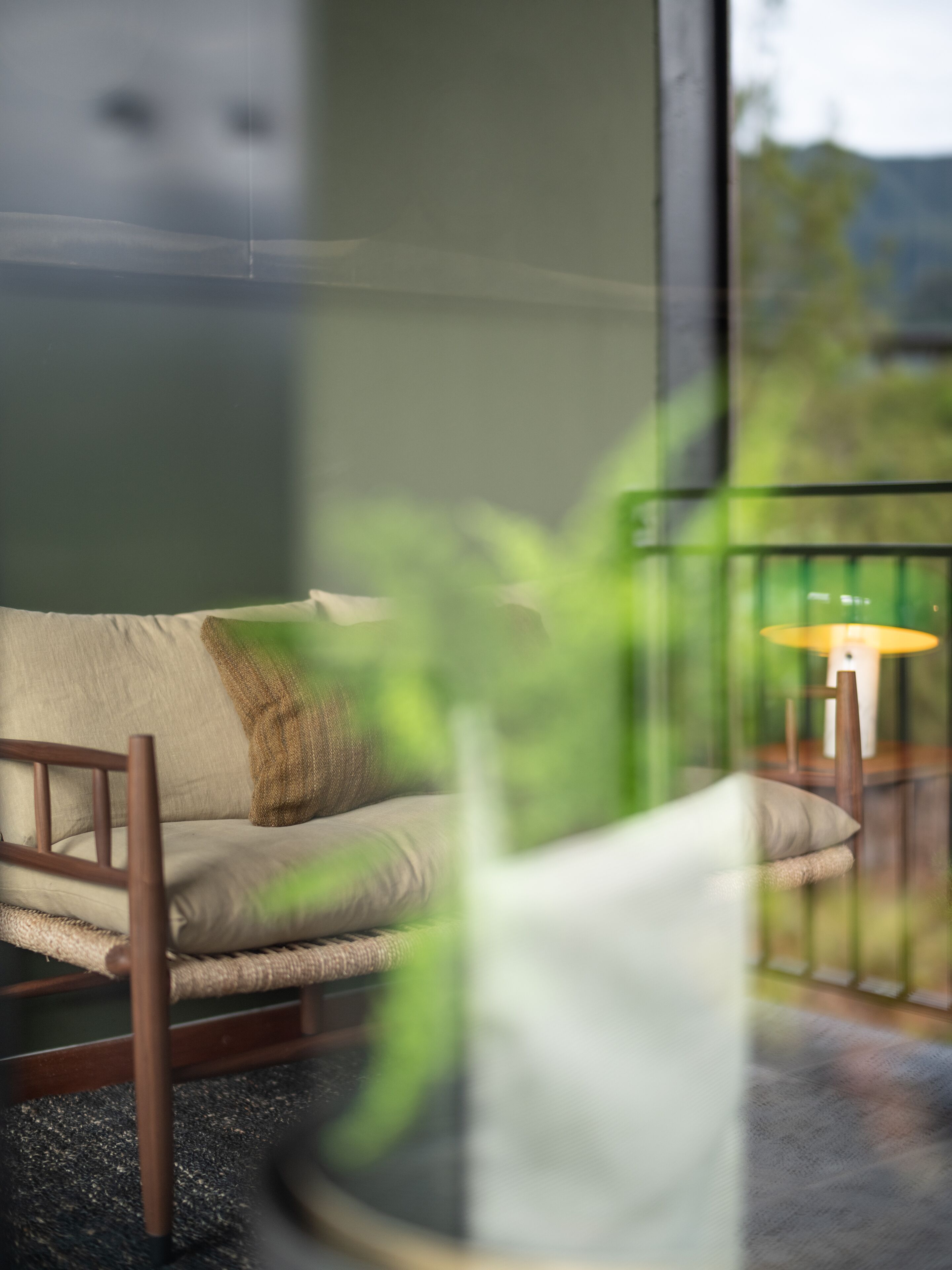 A room with a sofa, a lamp, and a view through a window.