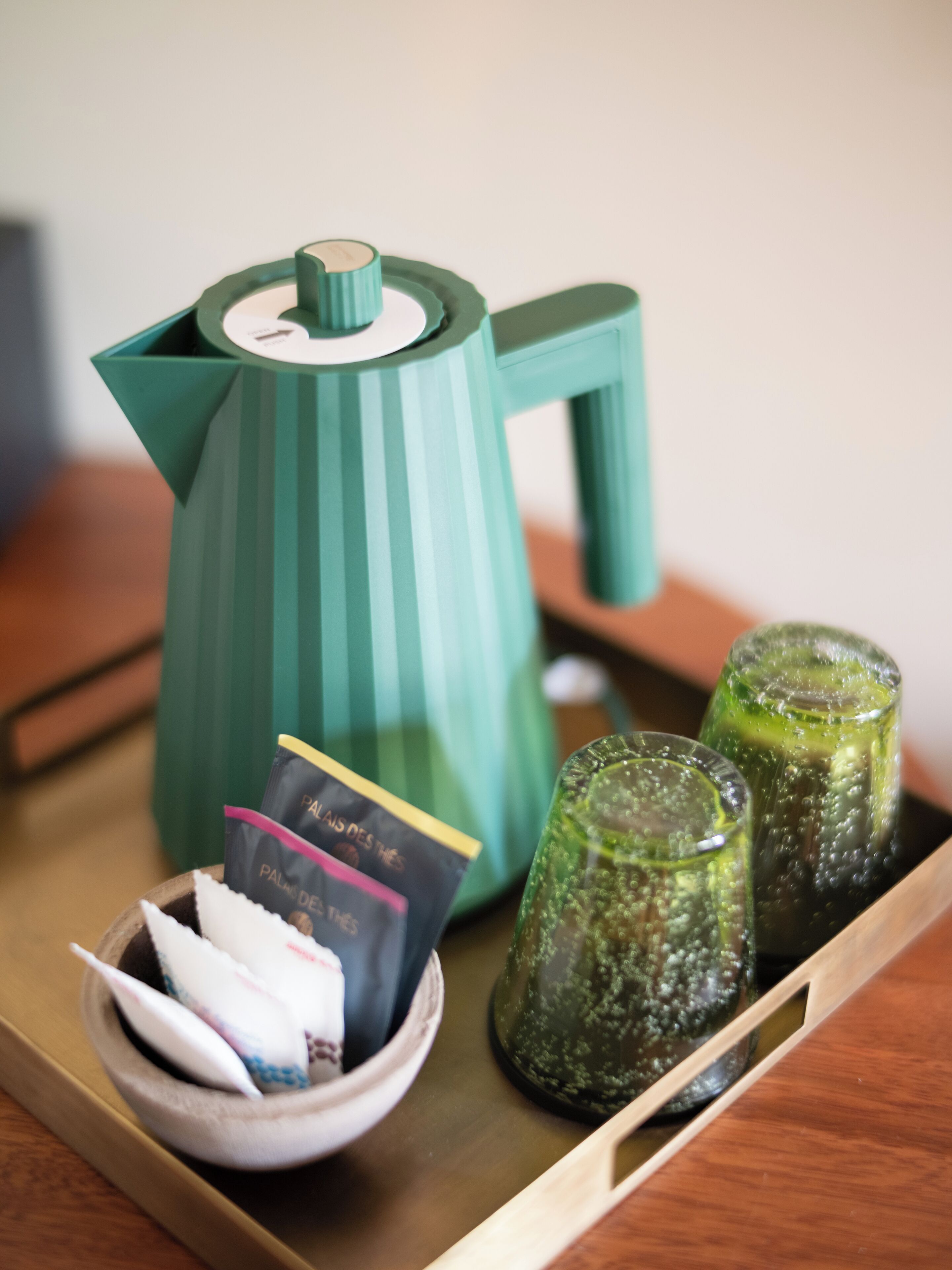 A teal-colored kettle, a bowl with tea bags, and two glass jars on a tray.