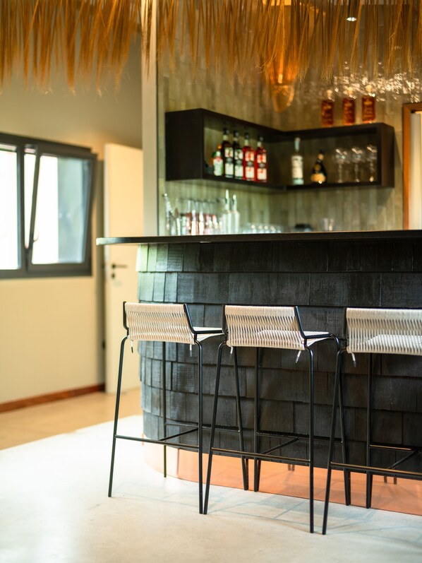 Una zona de bar con tres taburetes de mimbre y una barra negra.