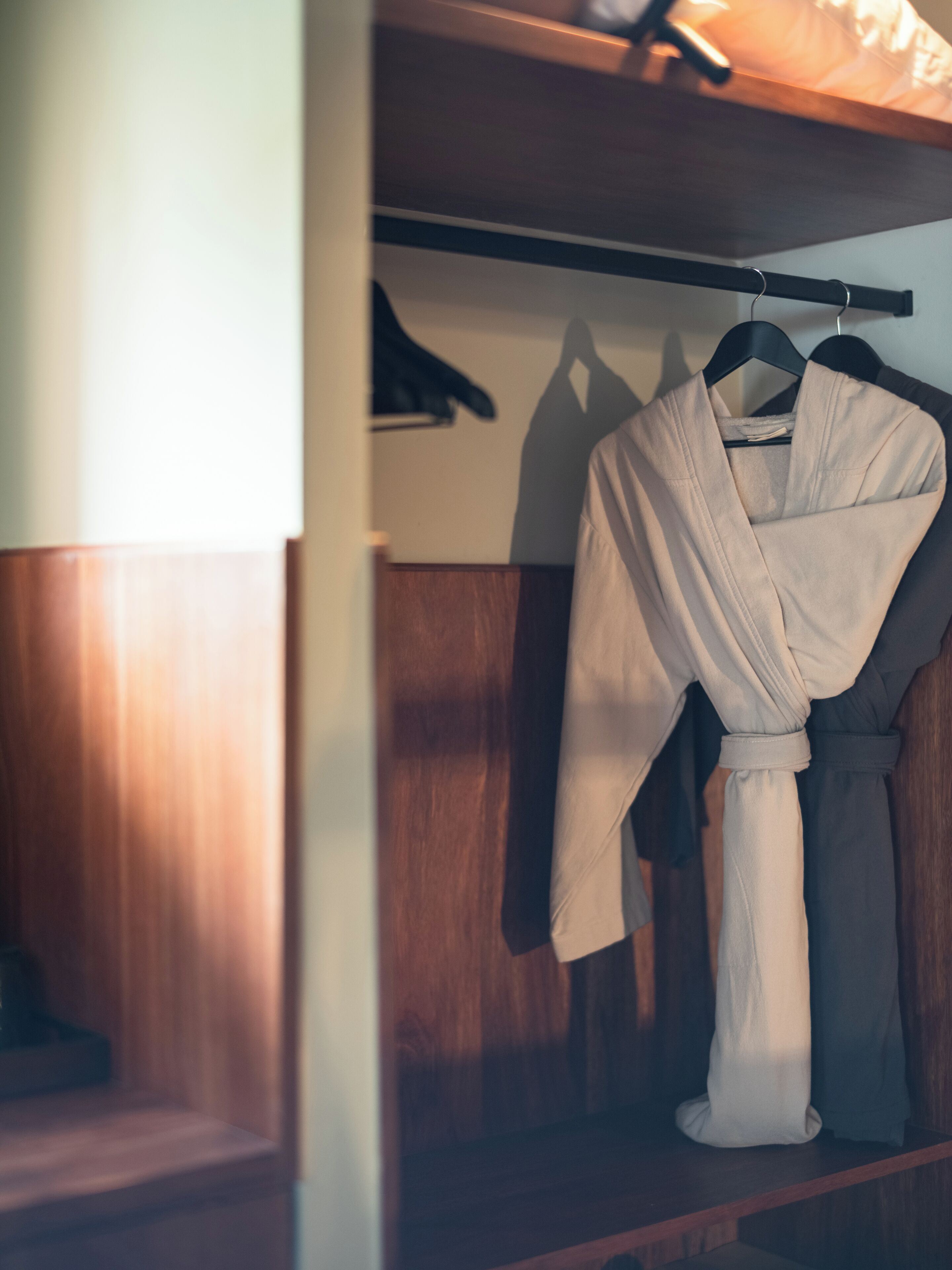 A wooden closet with a robe hanging on a rod.