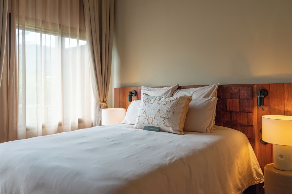 Una cama bien hecha con sábanas blancas, cabecera de madera y dos lámparas de noche.