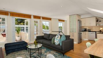 A modern living room with a sofa, a coffee table, and a dining area. There is a kitchen with cabinets and appliances.
