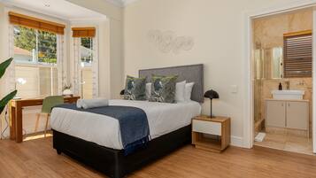 A bedroom with a large bed, bedside tables, a desk, and a chair. There is a bathroom with a sink and mirror.