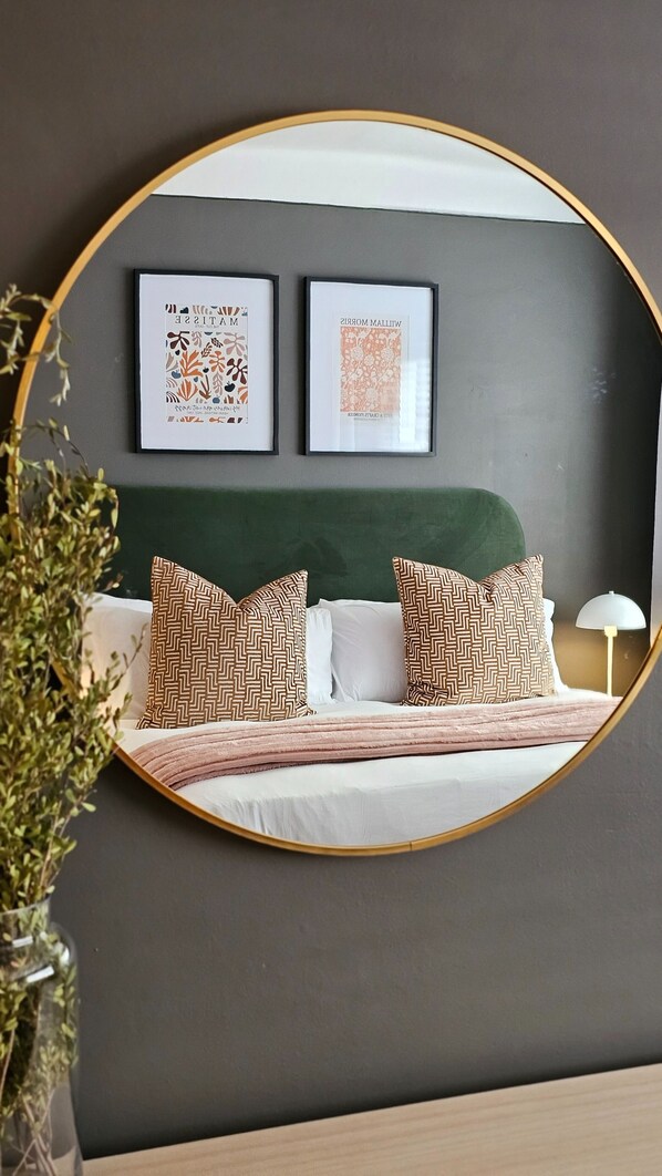 Un dormitorio con una cama, cabecera verde, dos cuadros enmarcados y almohadas estampadas.