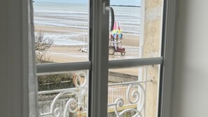 Vista desde una ventana sobre una playa con un velero y un tractor.