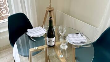 Een glazen tafel met een fles wijn, twee stoelen, een lamp en een raam met gordijnen.