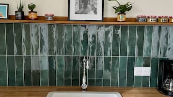 Cocina con pileta blanca, encimera de madera, salpicadero de azulejos verdes y un cuadro colgado sobre la pileta.
