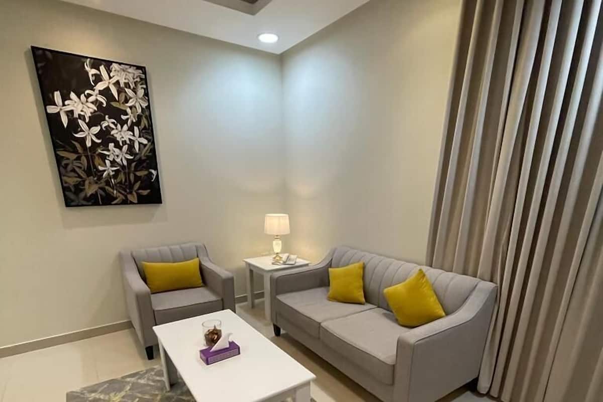 Een moderne woonkamer met een grijze bank, twee fauteuils, een witte salontafel en een vloerkleed met dessin.