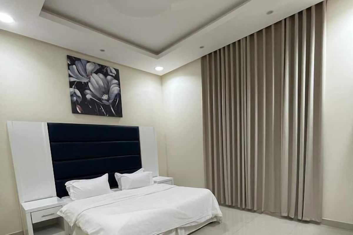Een moderne slaapkamer met een groot bed, een nachtkastje, een tv aan de muur en een plafondlamp.