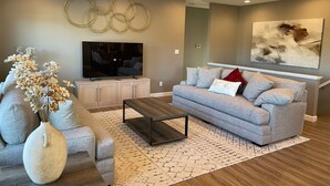 A modern living room with a grey sofa, a coffee table, a TV on a cabinet, and a vase with dried flowers.