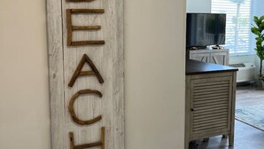 Una stanza con una decorazione a parete in legno che riporta la scritta 'BEACH' e un televisore su un mobile.