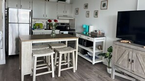 Una cucina moderna con mobili bianchi, un'isola in legno con sgabelli, un forno a microonde integrato e un televisore su un mobile in legno.