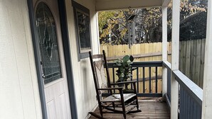 Une véranda en bois avec une chaise berçante, une petite table et une plante en pot.