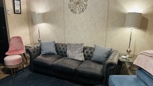Un salon moderne avec un canapé gris, des coussins à motifs, un fauteuil rose et un pouf bleu.