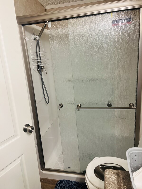 Ducha con cerramiento de vidrio, cabezal de ducha de mano y toallero.