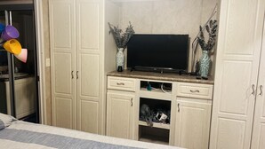 Une chambre à coucher avec un lit, un téléviseur posé sur un meuble en bois, et une salle de bain avec une porte en verre.