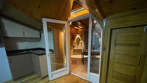 A cozy cabin interior with a wooden ceiling, a dining area with a table and chairs, and a kitchen with cabinets and a countertop.