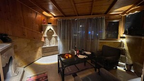 A cozy living room with a fireplace, a dining table set with a bottle, glasses, and fruit, and a sofa.